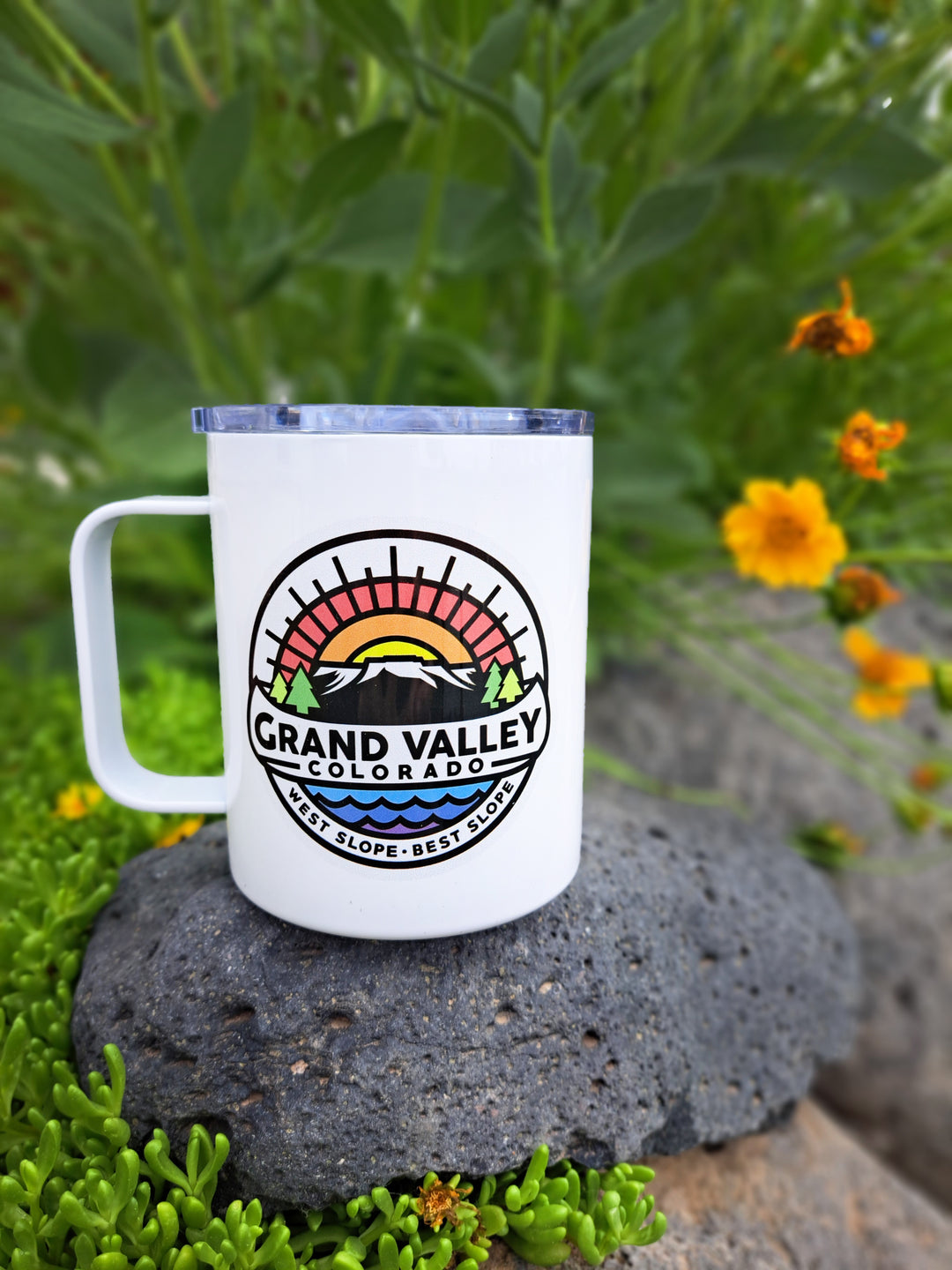 Coffee cup with spill-proof lid sitting on a rock with flowers beside it